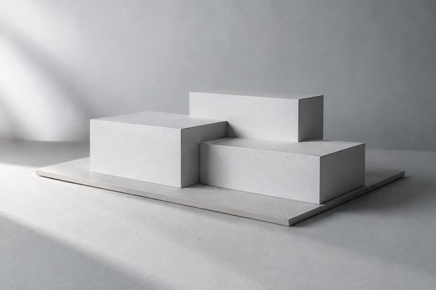 A plain white cardboard massing model of three simple blocks on a grey base