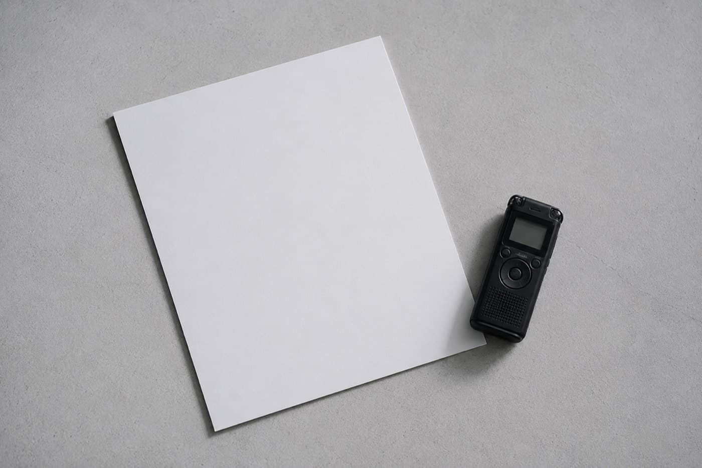 A blank sheet and a small recorder on a grey desk